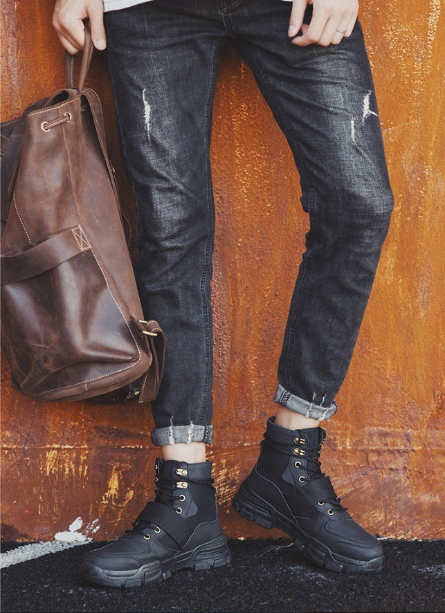 Stylish man wearing high quality winter boots with jeans and a brown bag against an orange background.